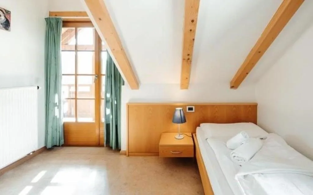 Camera luminosa con travi a vista in legno, letto e porta finestra con tende verdi