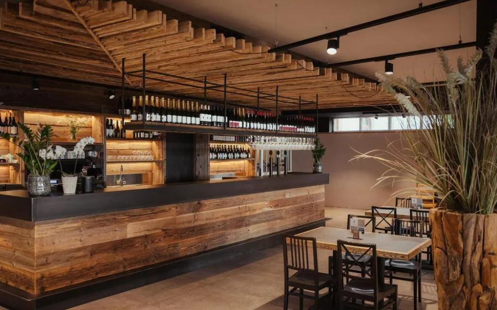 Bar dell'hotel con bancone e soffitto in legno rustico e bottiglie di vino esposte