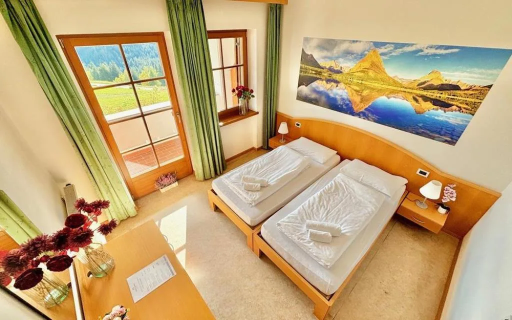 Camera doppia luminosa con vista sulle montagne, tende verdi e quadro decorativo