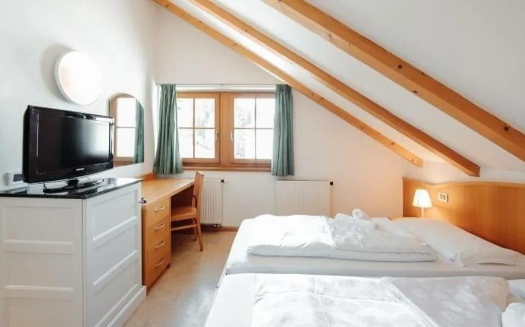 Camera mansardata con letto matrimoniale, televisore, scrivania e travi in legno