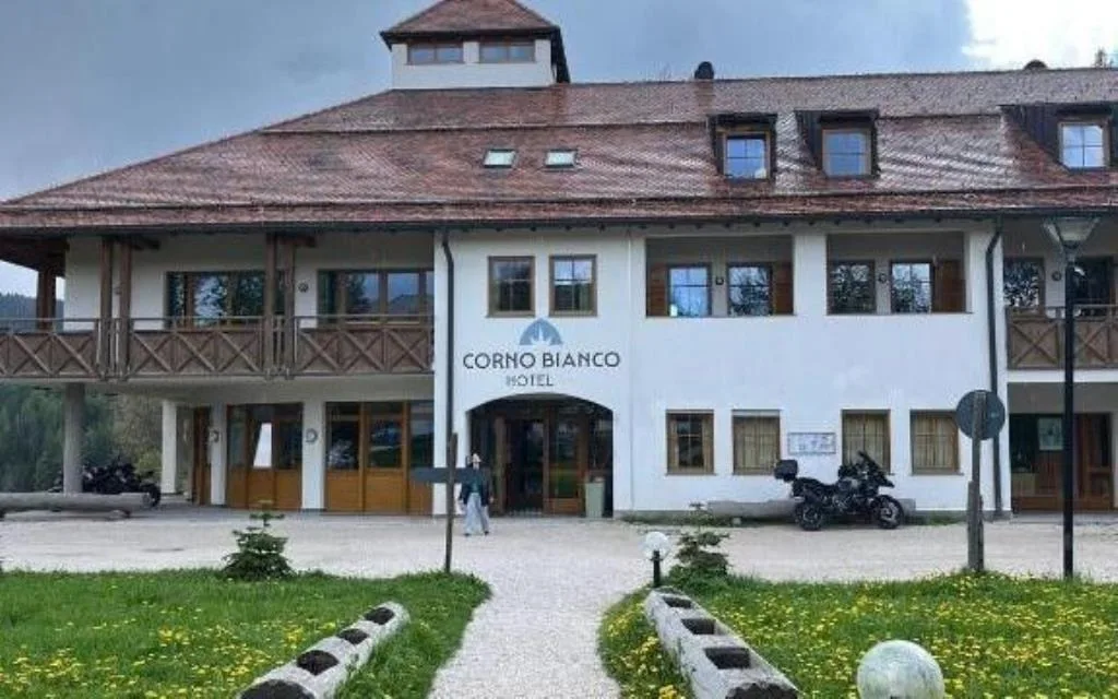 Facciata dell'Hotel Corno Bianco con giardino verde e cielo nuvoloso
