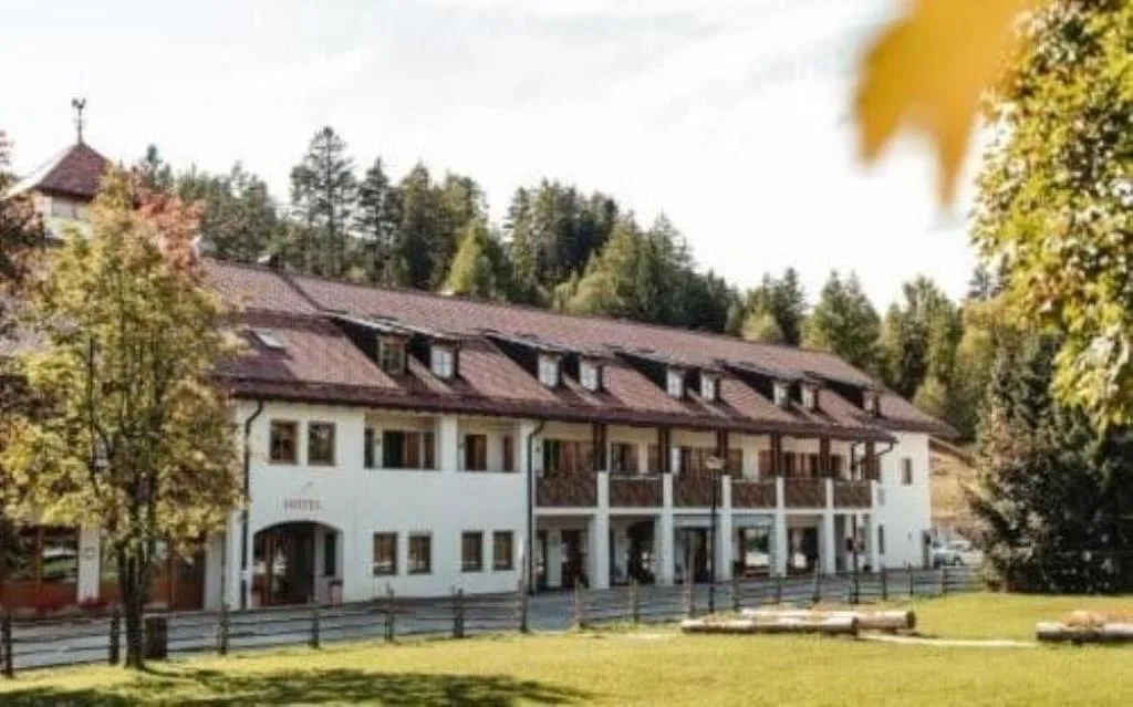 Esterno dell'hotel bianco con balconi in legno circondato da alberi autunnali