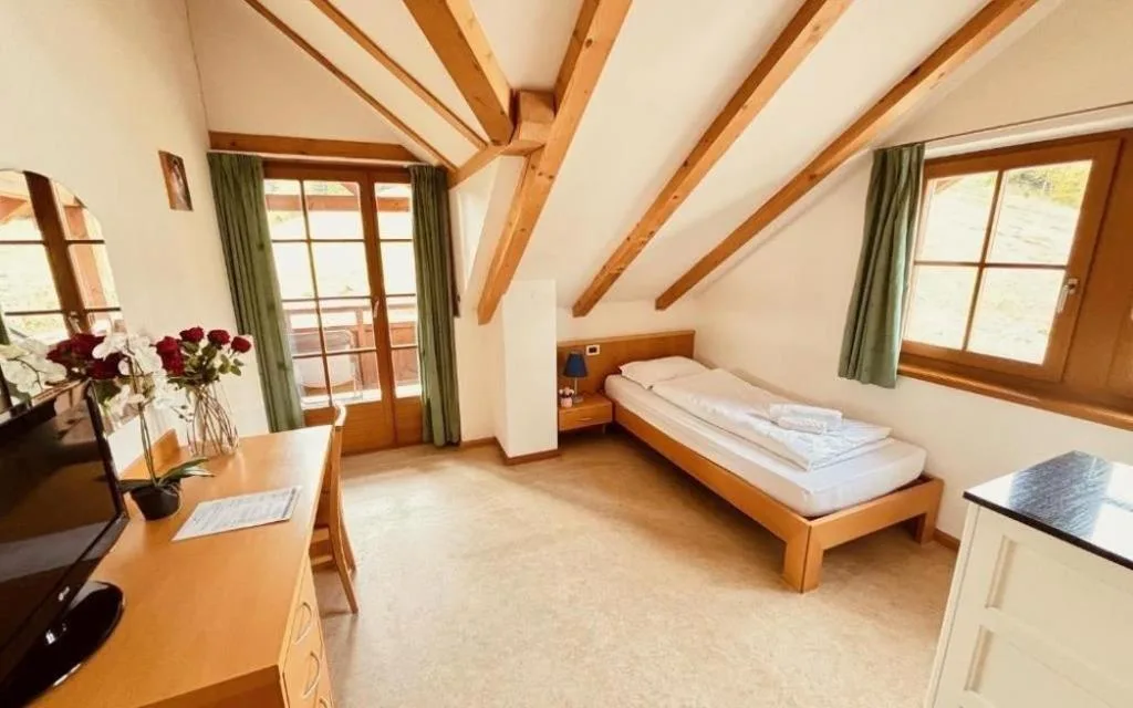 Camera mansardata con letto singolo, scrivania, travi in legno e porta balcone