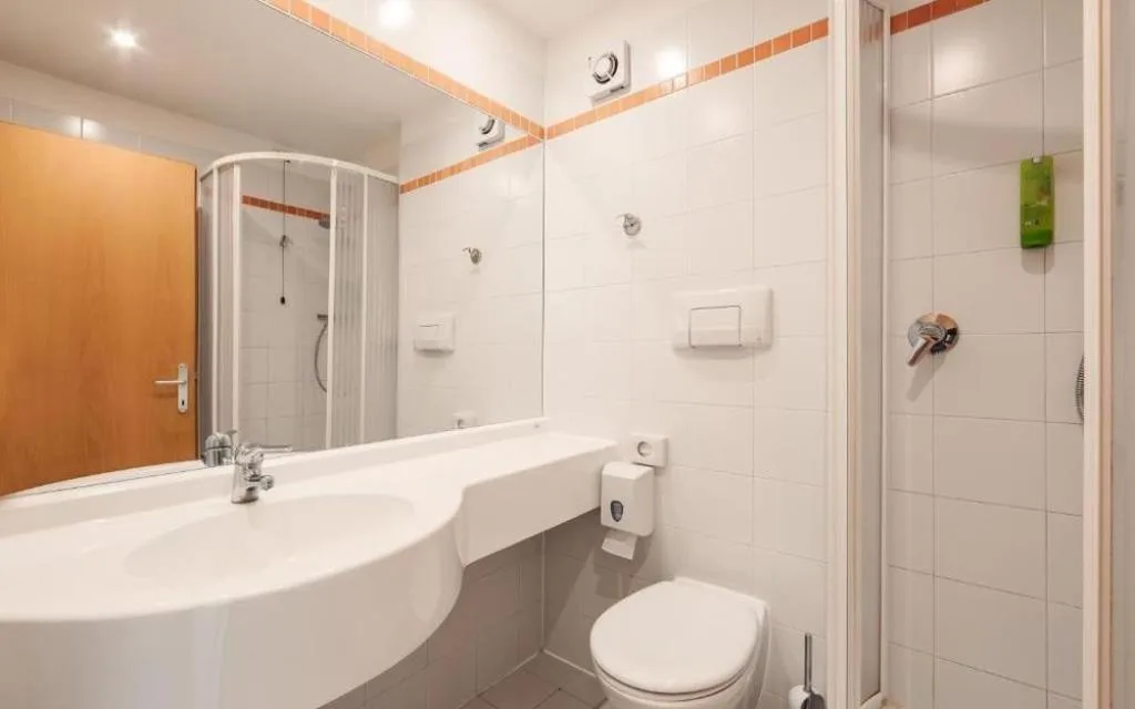 Bagno con doccia, lavabo con ampio specchio e WC in ambiente bianco luminoso
